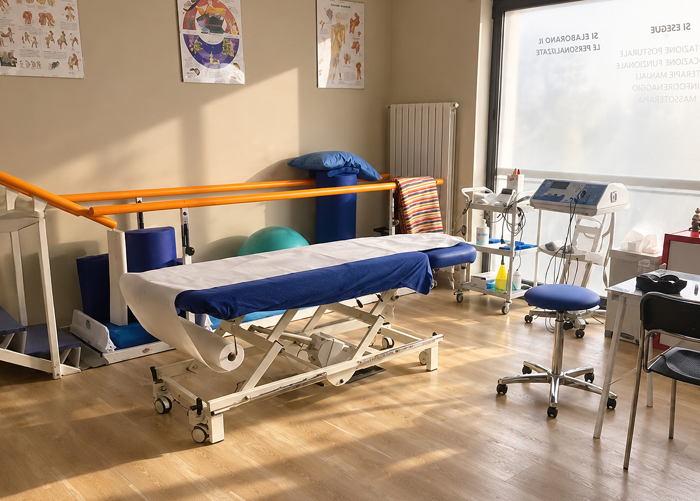 Sala trattamenti dello studio: lettino, parallele arancioni e poster anatomici